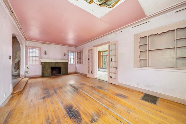 unfurnished living room with hardwood / wood-style flooring, a tile fireplace, crown molding, and french doors