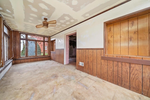 interior space with ceiling fan, wood walls, and crown molding