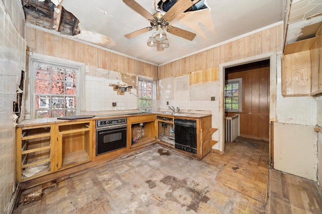 kitchen featuring sink, wood walls, black appliances, and a wealth of natural light