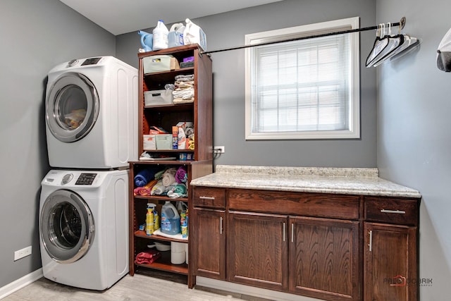 clothes washing area with light hardwood / wood-style floors, cabinets, and stacked washer / dryer