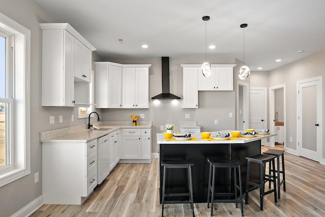 kitchen with white dishwasher, white cabinetry, wall chimney range hood, a kitchen island, and sink