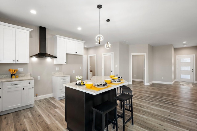 kitchen featuring light hardwood / wood-style floors, white cabinetry, a center island, and wall chimney range hood