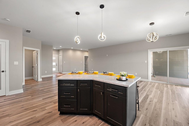 kitchen featuring decorative light fixtures, light stone counters, a center island, and light hardwood / wood-style flooring