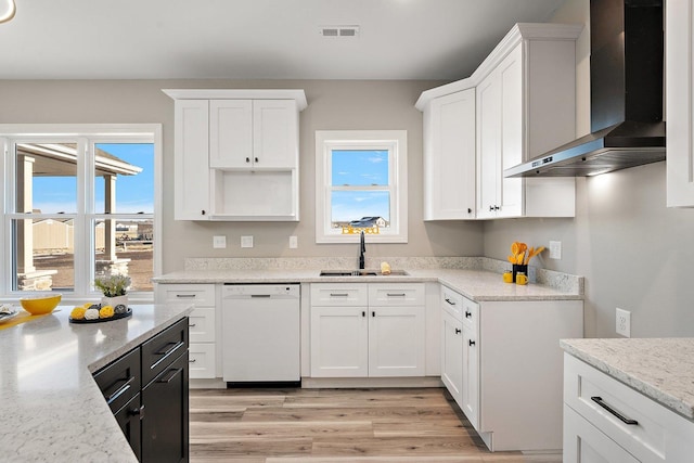 kitchen featuring dishwasher, wall chimney range hood, white cabinets, sink, and light stone counters