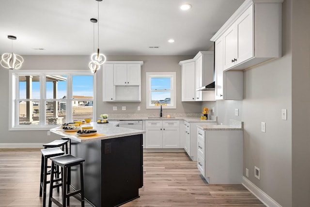 kitchen with white cabinets, a kitchen island, sink, hanging light fixtures, and light hardwood / wood-style flooring