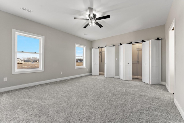 unfurnished bedroom featuring ceiling fan, a barn door, light colored carpet, and multiple windows