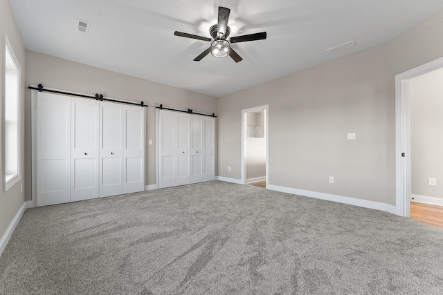 unfurnished bedroom featuring light carpet, connected bathroom, ceiling fan, and a barn door