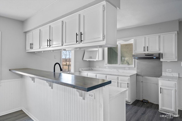 kitchen with a textured ceiling, a kitchen breakfast bar, white cabinets, kitchen peninsula, and dark hardwood / wood-style floors