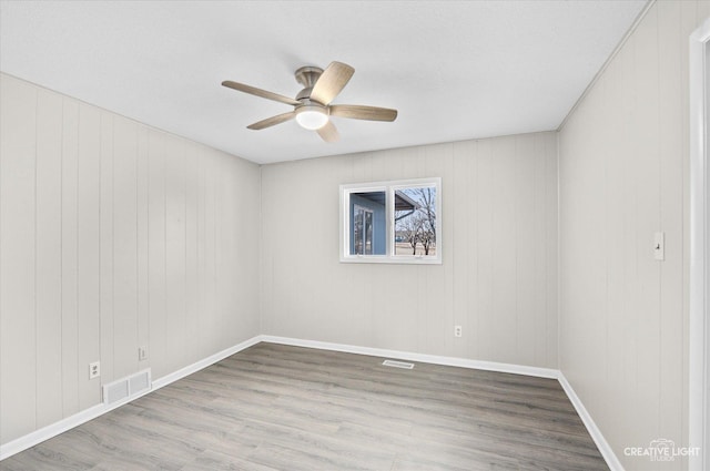 spare room featuring light hardwood / wood-style floors, ceiling fan, and wooden walls