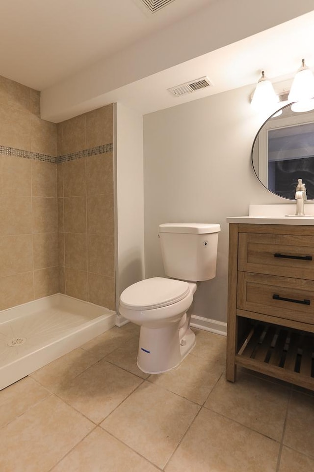 bathroom featuring toilet, vanity, tiled shower, and tile patterned flooring