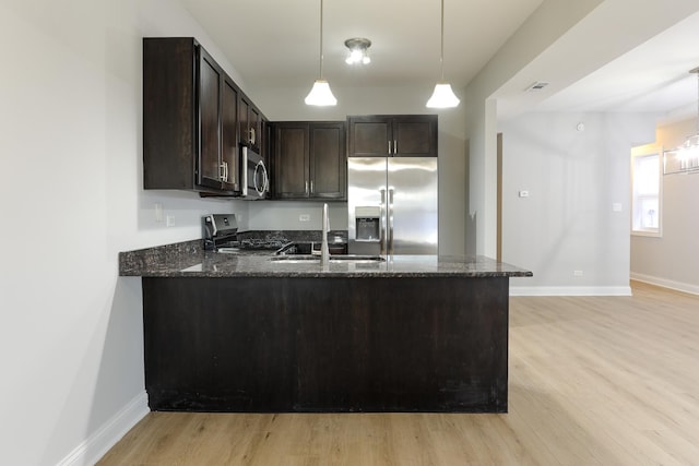 kitchen with dark brown cabinets, kitchen peninsula, stainless steel appliances, and dark stone counters