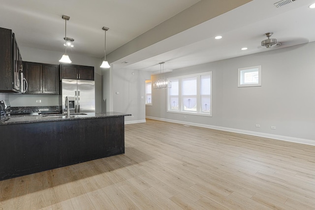 kitchen featuring dark brown cabinets, pendant lighting, dark stone countertops, light hardwood / wood-style floors, and stainless steel appliances