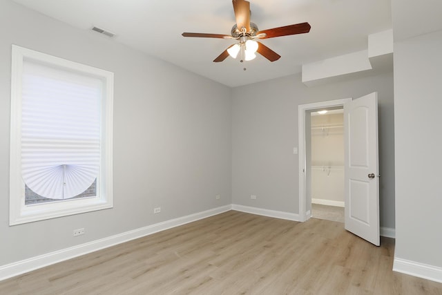 unfurnished bedroom featuring ceiling fan, a closet, a walk in closet, and light wood-type flooring