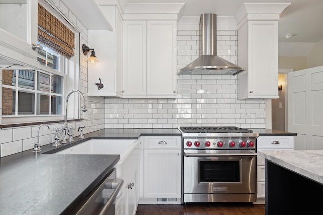 kitchen with appliances with stainless steel finishes, white cabinetry, sink, backsplash, and wall chimney range hood