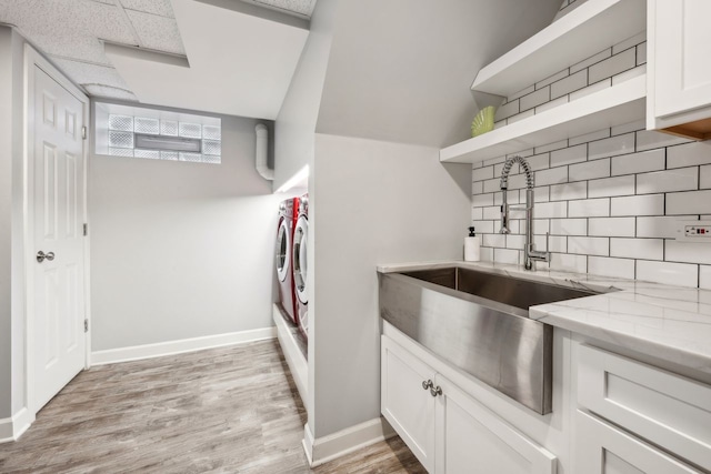 kitchen featuring sink, backsplash, washer and dryer, white cabinets, and light wood-type flooring