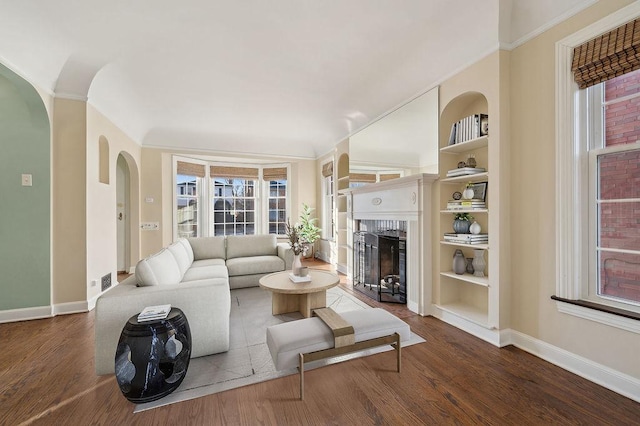 living room featuring built in shelves, ornamental molding, wood-type flooring, and a fireplace