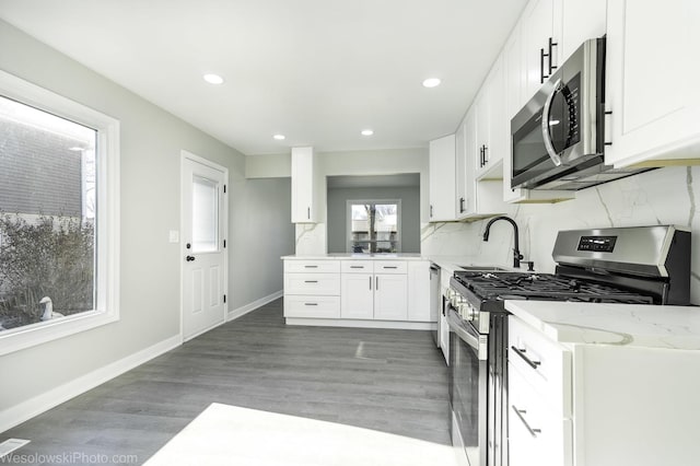 kitchen with sink, white cabinetry, wood-type flooring, stainless steel appliances, and light stone countertops