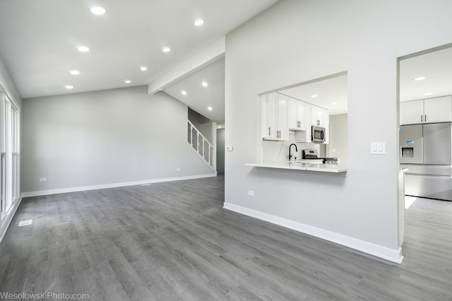 unfurnished living room with wood-type flooring, sink, and vaulted ceiling with beams