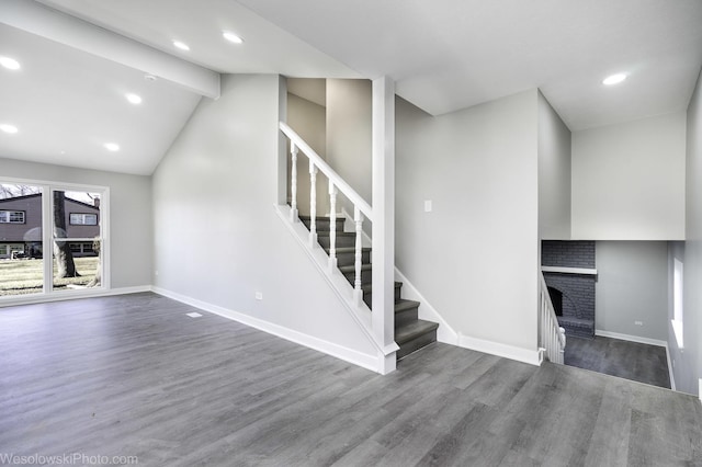 unfurnished living room with dark hardwood / wood-style floors, a brick fireplace, and vaulted ceiling with beams