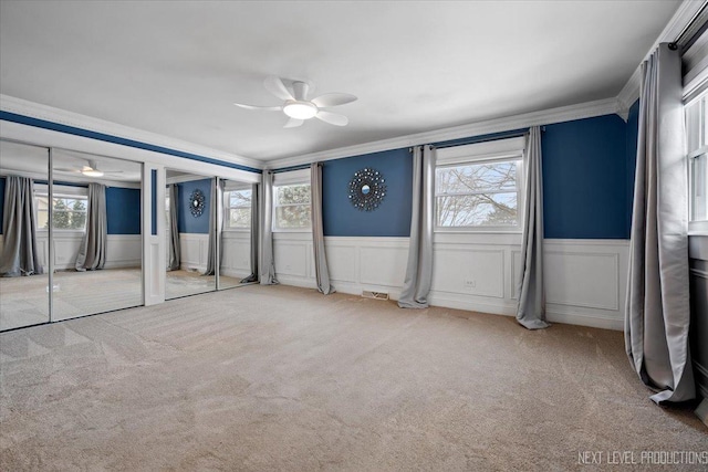 unfurnished bedroom featuring light carpet, two closets, ornamental molding, and ceiling fan