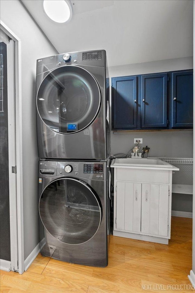 laundry room with light hardwood / wood-style floors, cabinets, and stacked washing maching and dryer