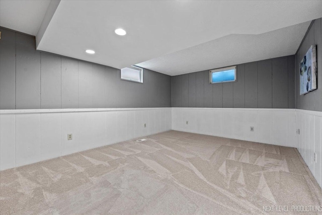 basement featuring light colored carpet and wooden walls