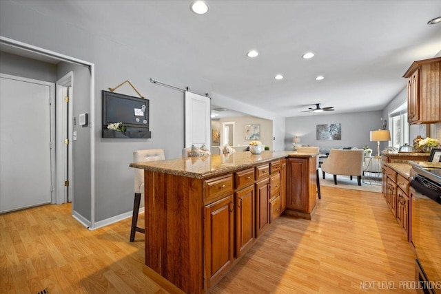 kitchen featuring a breakfast bar, a center island, a barn door, light stone countertops, and light hardwood / wood-style floors