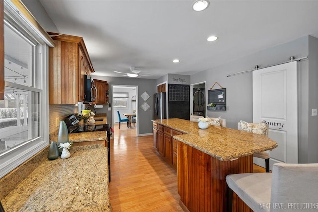 kitchen with light hardwood / wood-style flooring, appliances with stainless steel finishes, a kitchen island, a barn door, and light stone countertops