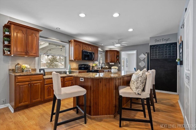 kitchen featuring tasteful backsplash, a breakfast bar area, light hardwood / wood-style floors, black appliances, and light stone countertops