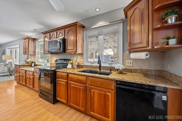 kitchen with sink, black appliances, light stone countertops, light hardwood / wood-style floors, and backsplash