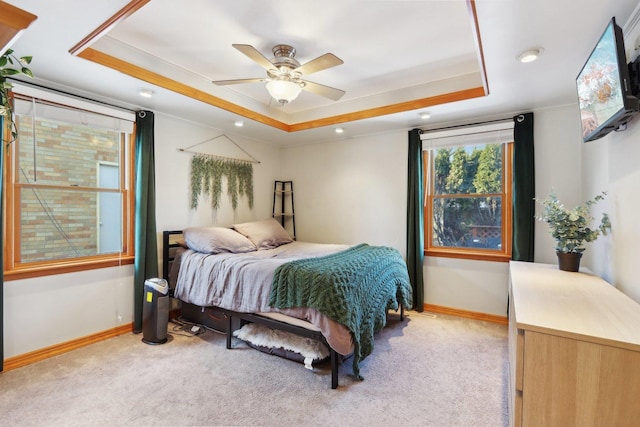 bedroom featuring light carpet, ceiling fan, and a tray ceiling