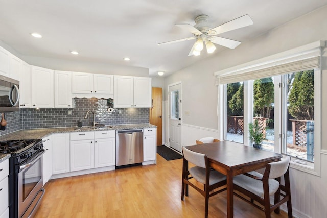 kitchen with sink, white cabinetry, stainless steel appliances, decorative backsplash, and dark stone counters