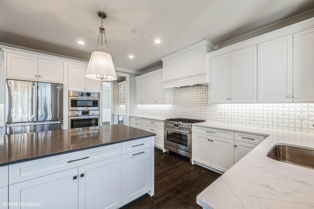 kitchen with light stone countertops, appliances with stainless steel finishes, hanging light fixtures, white cabinets, and sink