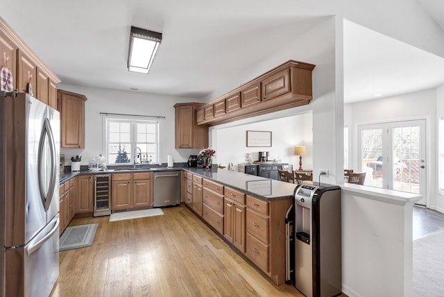 kitchen featuring stainless steel appliances, a sink, dark stone counters, beverage cooler, and a peninsula