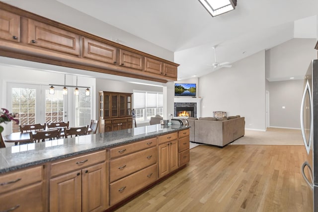 kitchen with pendant lighting, brown cabinetry, open floor plan, vaulted ceiling, and a warm lit fireplace