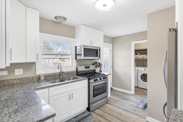 kitchen featuring sink, appliances with stainless steel finishes, white cabinetry, dark stone countertops, and light wood-type flooring