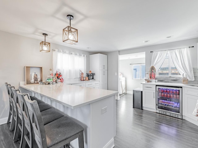 kitchen featuring a breakfast bar, pendant lighting, white cabinets, beverage cooler, and kitchen peninsula