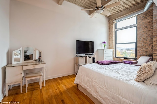 bedroom featuring multiple windows, light hardwood / wood-style flooring, ceiling fan, and brick wall