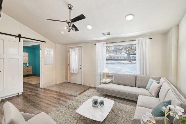 living room with ceiling fan, a barn door, lofted ceiling, and light hardwood / wood-style floors