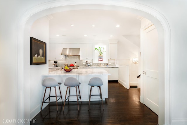 kitchen featuring a breakfast bar area, white cabinets, decorative backsplash, exhaust hood, and light stone counters