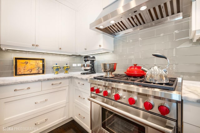 kitchen featuring wall chimney range hood, white cabinetry, designer range, light stone countertops, and decorative backsplash