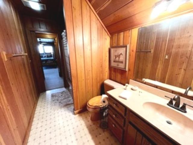 bathroom with lofted ceiling, wood ceiling, vanity, toilet, and wood walls