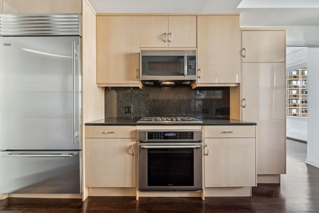 kitchen featuring dark stone countertops, stainless steel appliances, dark hardwood / wood-style flooring, decorative backsplash, and light brown cabinets