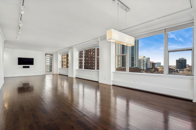 unfurnished living room with plenty of natural light, track lighting, and dark hardwood / wood-style flooring