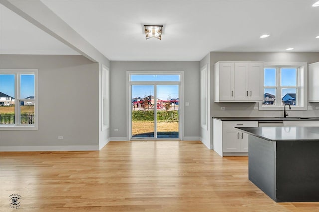 kitchen featuring baseboards, a sink, light wood-style floors, white cabinetry, and dark countertops