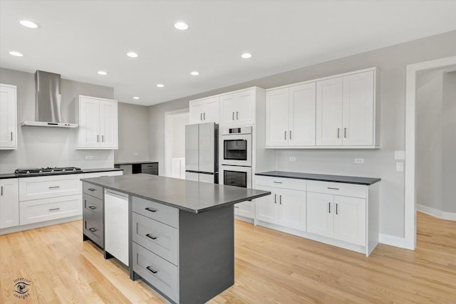 kitchen with wall chimney exhaust hood, light hardwood / wood-style floors, white cabinetry, and appliances with stainless steel finishes