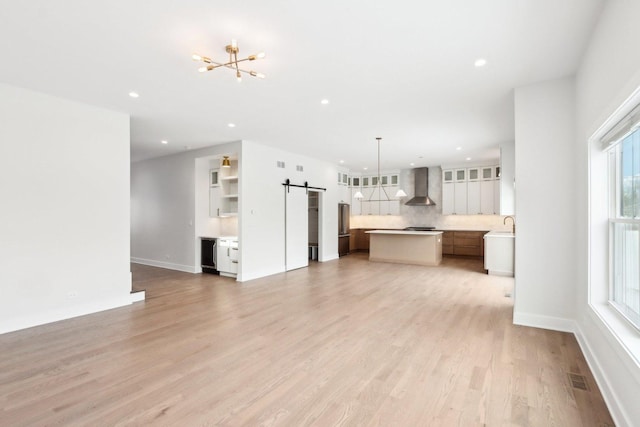 unfurnished living room featuring an inviting chandelier, a barn door, and light hardwood / wood-style flooring