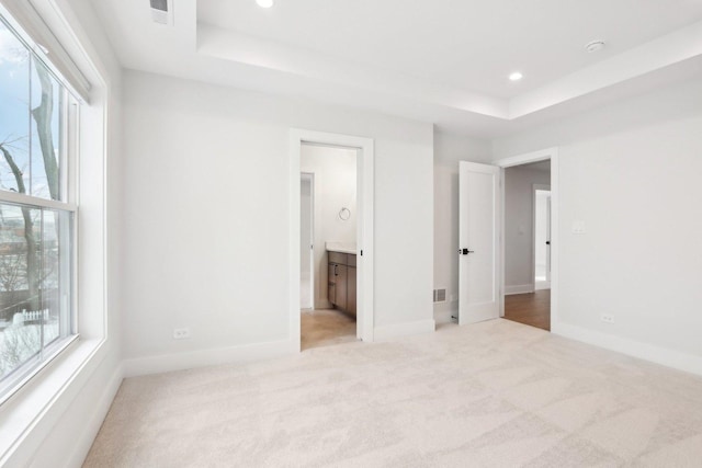 unfurnished bedroom with light carpet, a tray ceiling, and ensuite bathroom