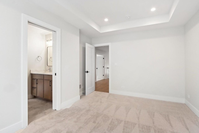 unfurnished bedroom featuring a raised ceiling, sink, light carpet, and ensuite bath