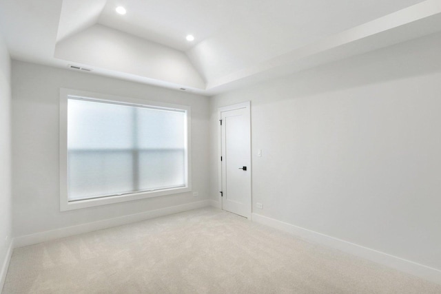 carpeted empty room featuring a tray ceiling and vaulted ceiling